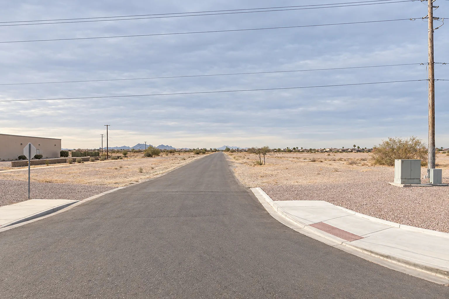 Flat desert lot at a suburban intersection in Arizona City, with utility poles along the roadside