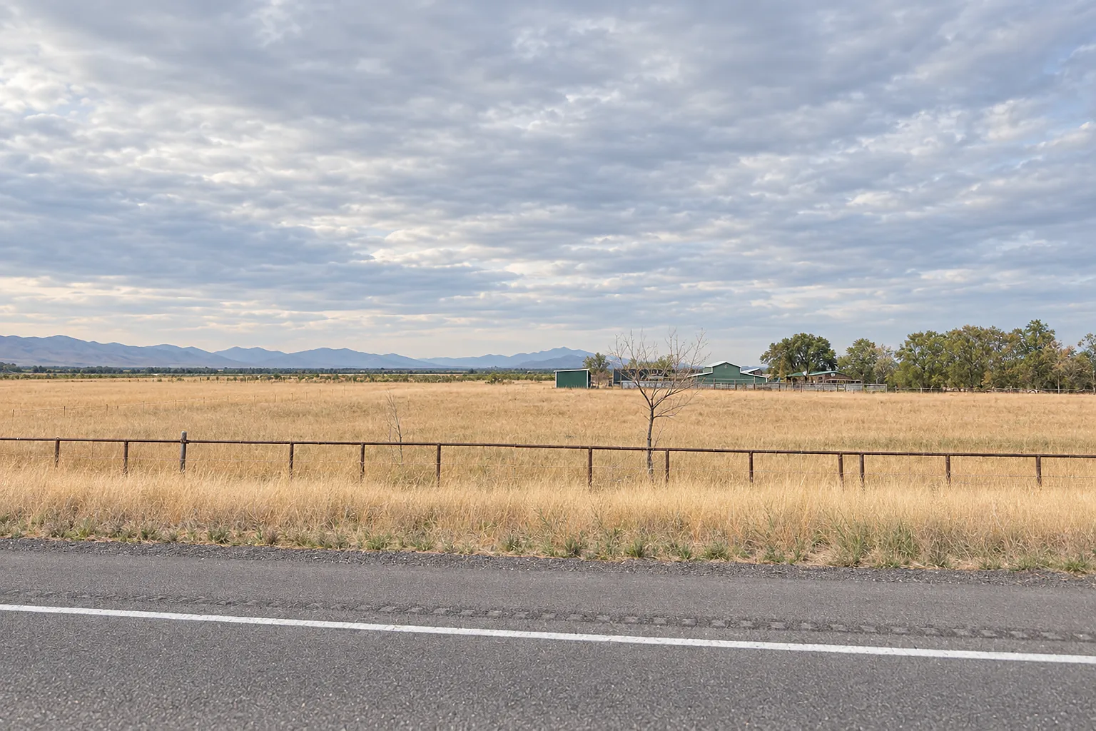 Hay field beside a two-lane state highway east of Grantsville, with a distant farmstead and mountains